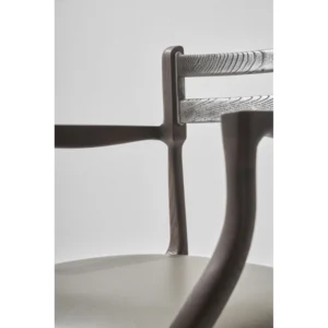 Close-up view of a District Eight Assembly Dining Chair with Armrests showcasing the chair’s design details such as the wood grain texture, joint connections, and the contrast of metal accents against the dark wood finish