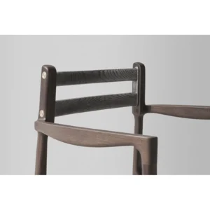Close-up view of a District Eight Assembly Dining Chair with Armrests showcasing the chair’s design details such as the wood grain texture, joint connections, and the contrast of metal accents against the dark wood finish